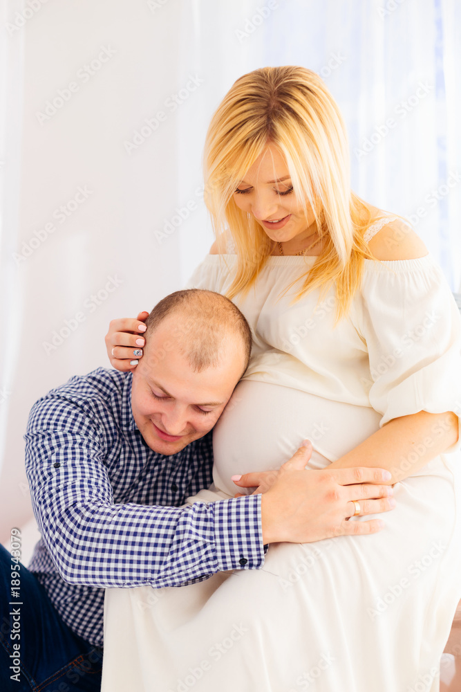 A man in a stylish shirt sits next to his pregnant wife and puts A man in a stylish shirt sits next to his pregnant wife and puts