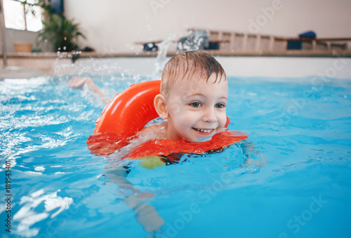 Portrait of happy white Caucasian child in swimming pool. Preschool boy training to float with red circle ring in water. Healthy active lifestyle