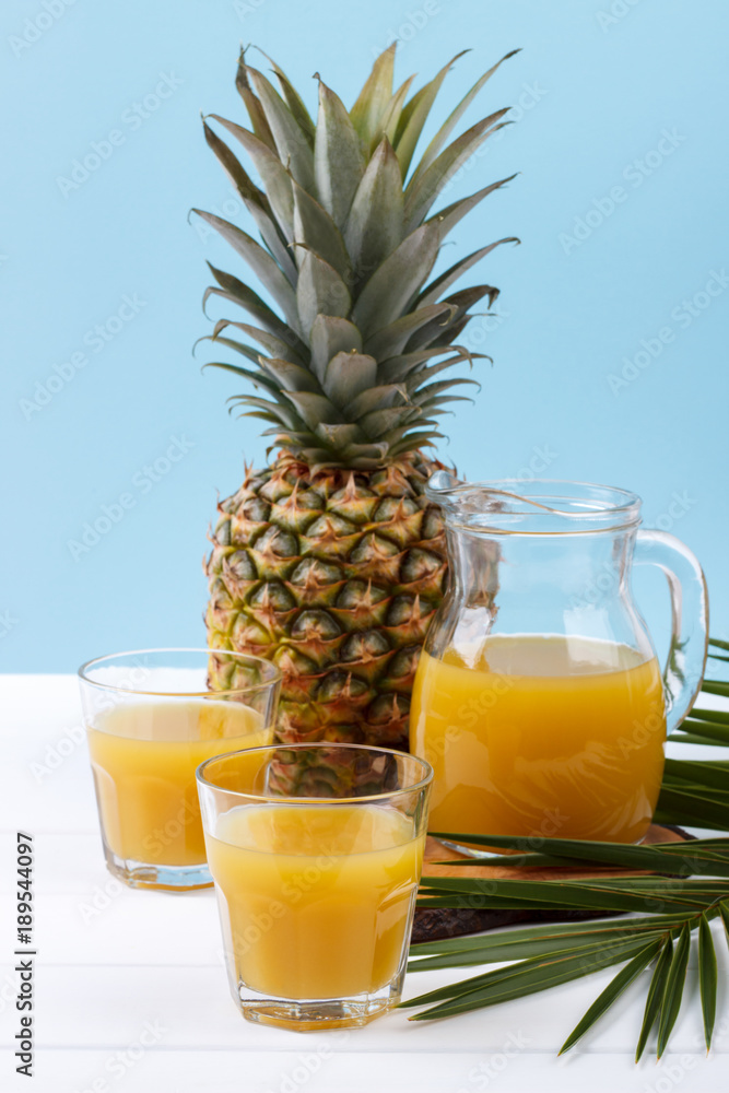 glass and pitcher of pineapple juice and whole fruit on blue background glass and pitcher of pineapple juice and whole fruit on blue background