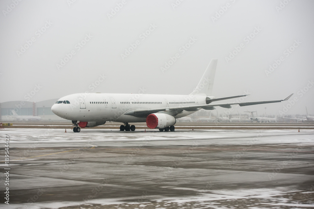 Large wide-body passenger airplane standing on the apron on the parking place of international airport during snow blizzard Large wide-body passenger airplane standing on the apron on the parking place of international airport during snow blizzard