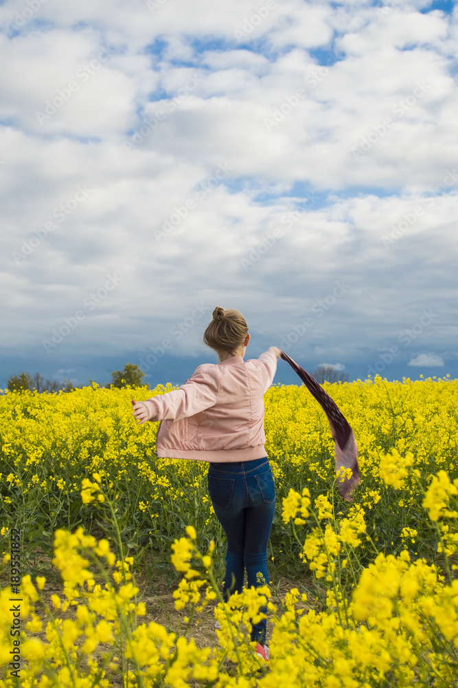 Happy, independent, girl runs in the field with rapeseed in windy weather waving waving scarf Happy, independent, girl runs in the field with rapeseed in windy weather waving waving scarf