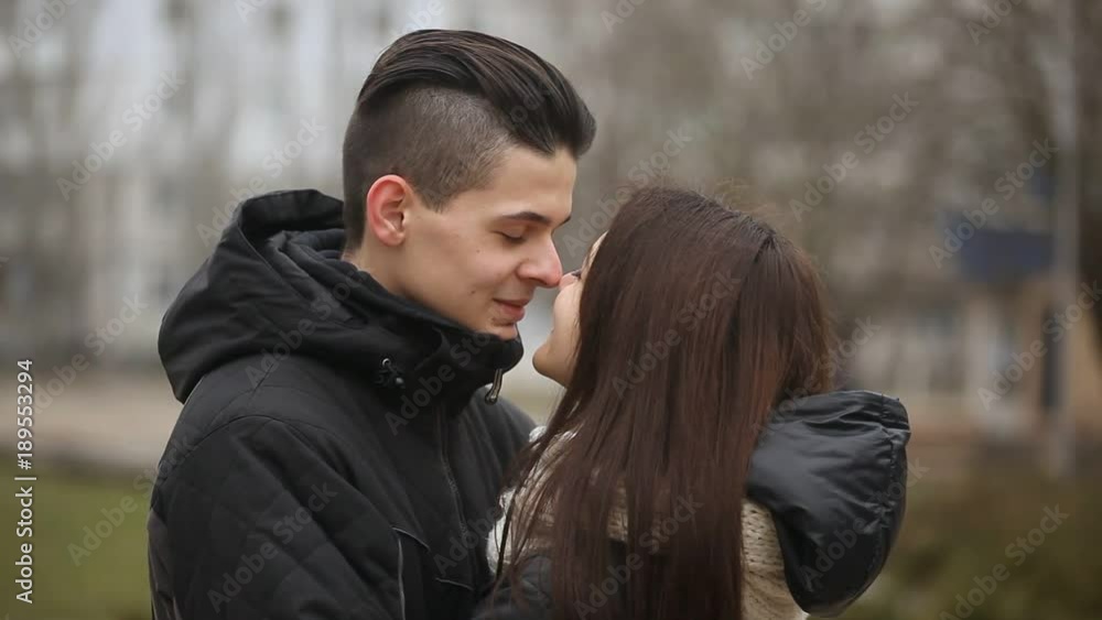 A cheerful view of a young pair smiling and pressing the tips of their noses. Their Escimo kiss looks romantic on a city street in winter A cheerful view of a young pair smiling and pressing the tips of their noses. Their Escimo kiss looks romantic on a city street in winter
