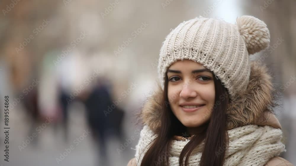 An optimistic closeup of a smiling girl with long loose hair in an anorak and a knitted hat with funny balls on an alley in winter An optimistic closeup of a smiling girl with long loose hair in an anorak and a knitted hat with funny balls on an alley in winter