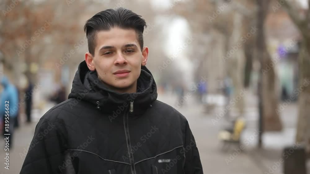 A magnificent view of a young brunette man with a crew haircut in a black anorak. He stands on a picturesque white alley in winter A magnificent view of a young brunette man with a crew haircut in a black anorak. He stands on a picturesque white alley in winter