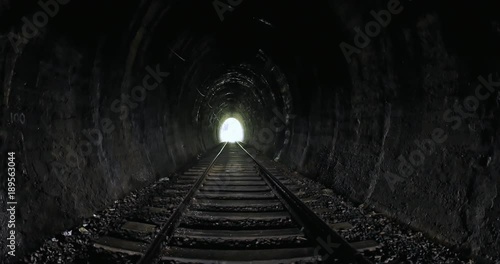 View from inside of old dark long railroad tunnel with bright light in the end