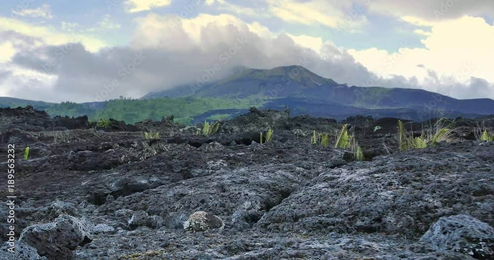 Exploring crater of Batur volcano. Black lava stones and rocks nature landscape background and scenic Bali landmark