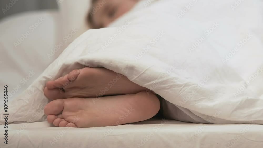 Female scratching her foot under white blanket, allergy medical treatment need Female scratching her foot under white blanket, allergy medical treatment need