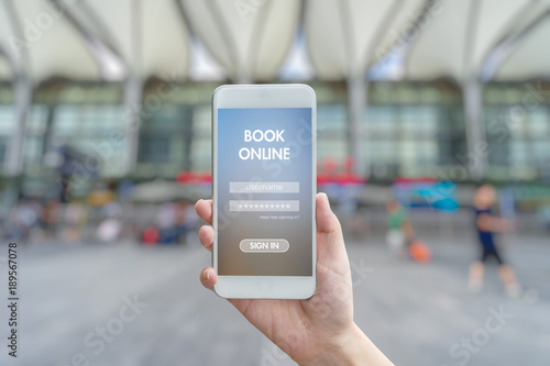 Woman hand holding smartphone against blur bokeh of station background BOOK online concept