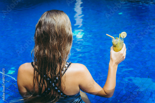 Beautiful woman is drinking a cocktail near swimming pool