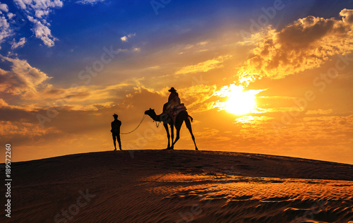 Desert sunset at Jaisalmer Rajasthan with tourist on camel in silhouette effect and moody sky.