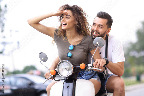 Beautiful young couple is smiling while riding a scooter © ASDF