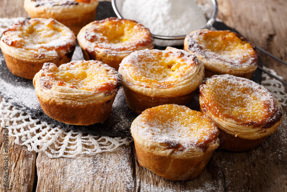 Delicious Pastel de Nata cakes stuffed with custard, sprinkled with powdered sugar close-up on the table. horizontal
