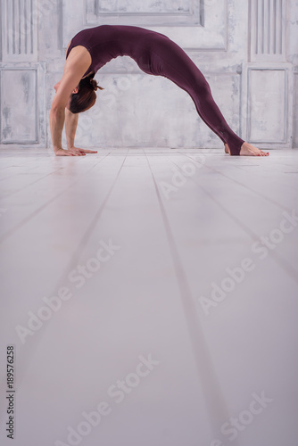 Young woman doing yoga Bridge pose. Asana Chakrasana or Dhanurasana. Sporty young woman doing yoga practice on light background.