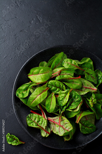 Fresh young leaves of chard for salad in a dark ceramic dish on black concrete background. Selective focus. Copy space. Top view.