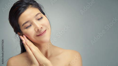 Happy beautiful asian girl with the fresh skin and relaxing in grey colour background. Expressive facial expressions. Cosmetology and Spa concept.