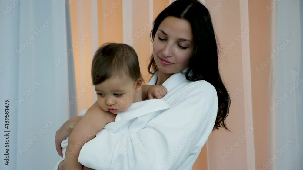 woman in white Bathrobe holding son in her arms in bright bedroom woman in white Bathrobe holding son in her arms in bright bedroom