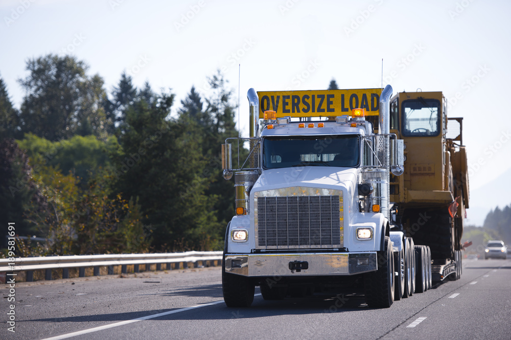 Big rig semi truck with oversize load sign and step down trailer carry and transporting digger