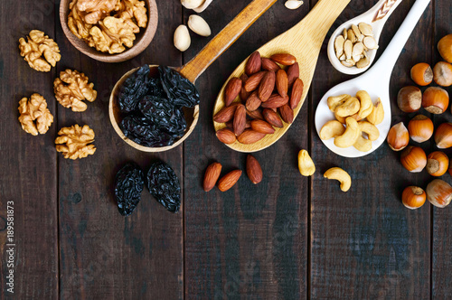 Assorted different nuts, prunes, pumpkin seeds in spoons on a dark wooden background. Top view.