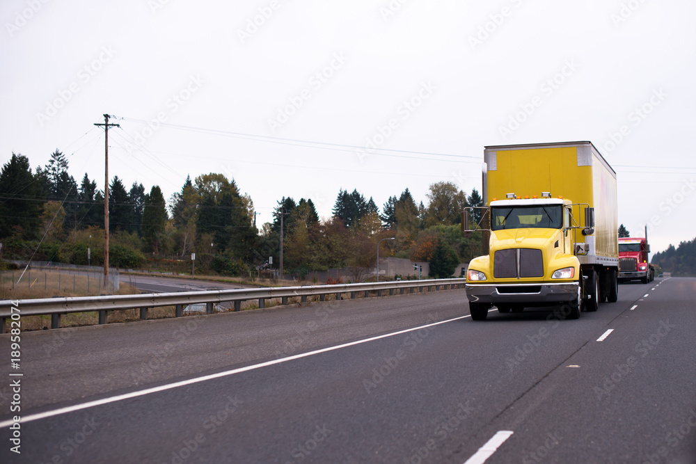 Yellow big rig semi truck with box trailer for safety transporting goods moving on wide highway