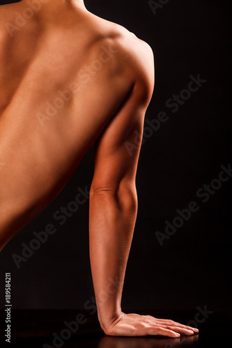 Arm and part of back of muscular woman posing against black background