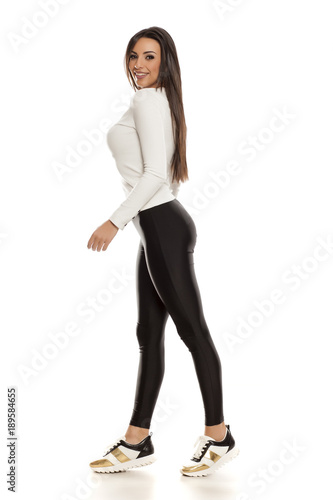 Profile of young beautiful woman in black tights, white blouse and sneakers on white background