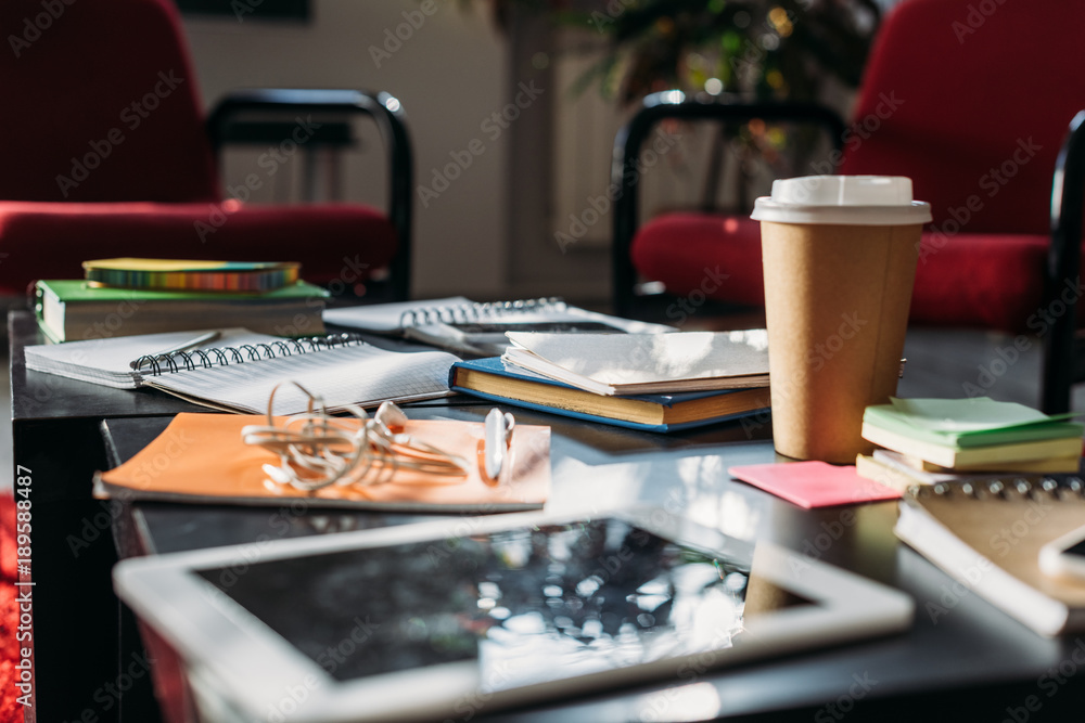 tablet with disposable coffee cup and notebooks on table tablet with disposable coffee cup and notebooks on table