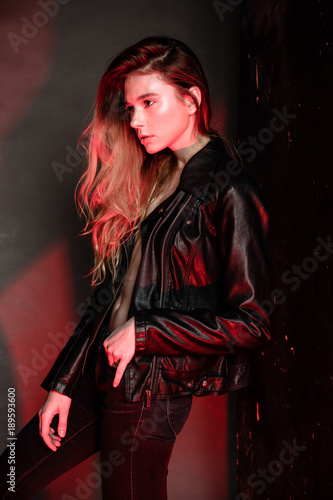 sexy blonde woman in leather clothes posing against grey studio wall