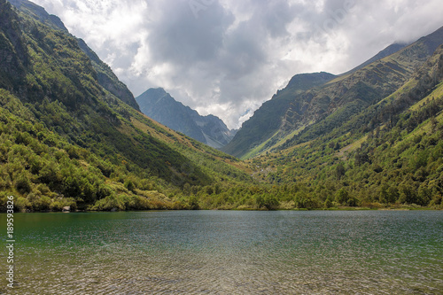 mountain gorge in summer, green trees and a lake in the Caucasus, Dombay with clouds in the sky © Ambartsumian