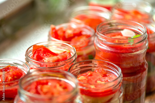 Canning fresh tomatoes with onions for winter in jelly marinade. Macro shot of basil leaves on top of a red ripe tomato slice being put in jar.