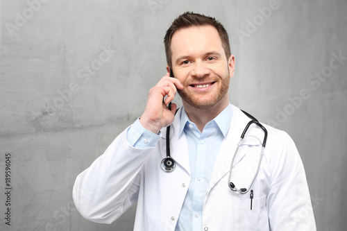 Lekarz rozmawia przez telefon. Przystojny lekarz ubrany w biały kitel stoi w klinice i rozmawia przez telefon 