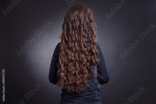 head of a brown-haired with curly long hair on dark background isolated rear view