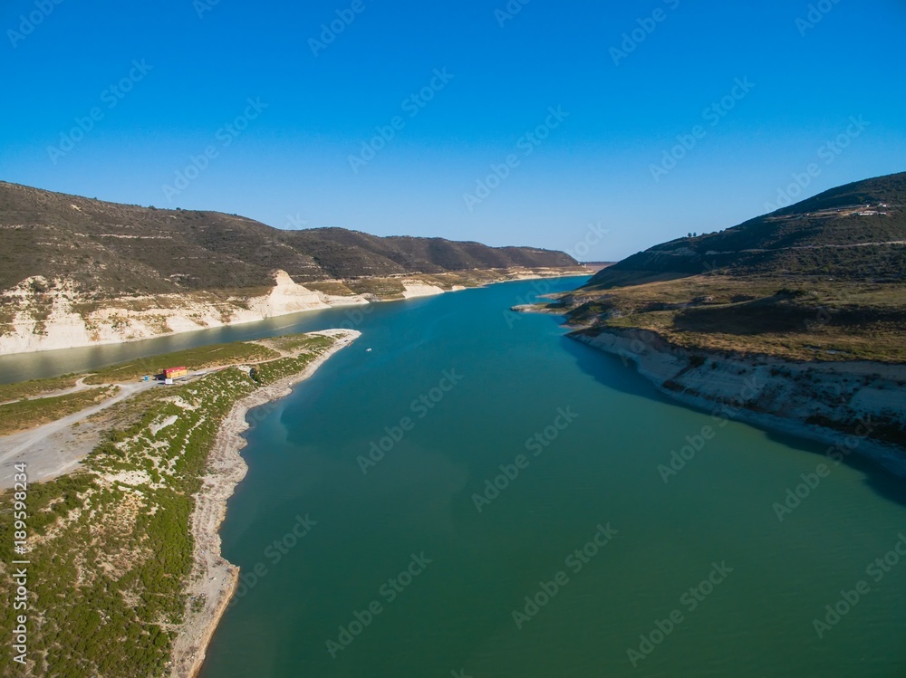Aerial Bird's eye view of artificial lake at the largest dam in Cyprus, Kouris reservoir, Limassol. View of the river split peninsula, earthfill embankment and hills around water from above.