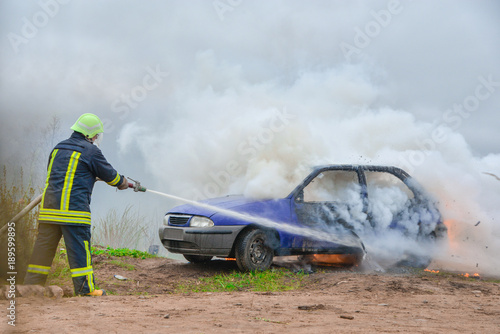 Fire fighter prepare to attack a propane fire. Burning and crashed car after explosion. Accident on street at countryside. No one was injured. Artificially created set for film making.
