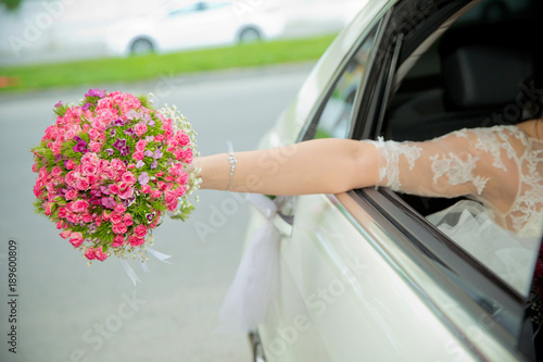 The bride took out the pink flower bouquet out of the car . bride girl goes to wedding cars and waving with a bouquet out of it. The bride's bouquet of flowers. Wedding day.