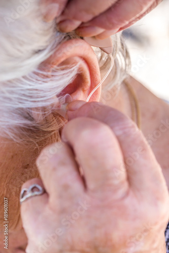 senior woman inserting hearing aid in her ears