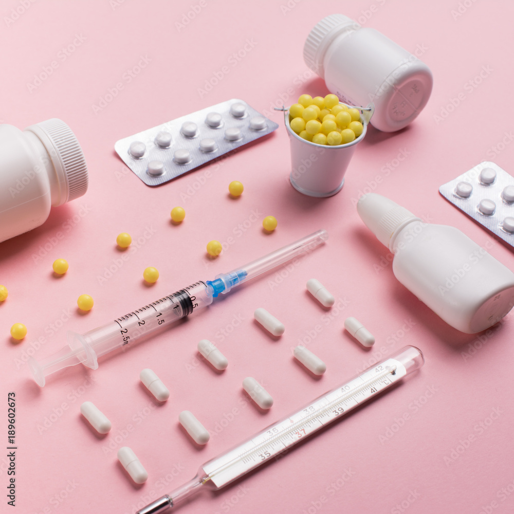 Creative concept Illness: thermometer, syringe, vitamins and tablets in a jar on pink background Creative concept Illness: thermometer, syringe, vitamins and tablets in a jar on pink background