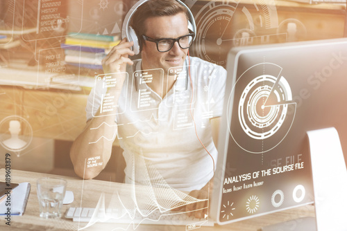 Smart software. Cheerful IT man wearing headphones and using his computer while workign on security program photo