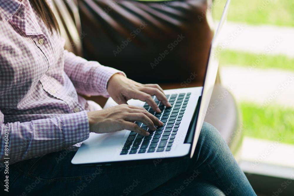 Naklejka premium Freelancing woman using laptop computer for distance job while sitting in coffee shop. Business woman typing on laptop at workplace Woman working in home office hand keyboard.