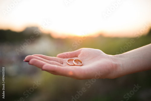 Golden wedding rings in hands of woman on a sunset background. Wedding details  © Yana