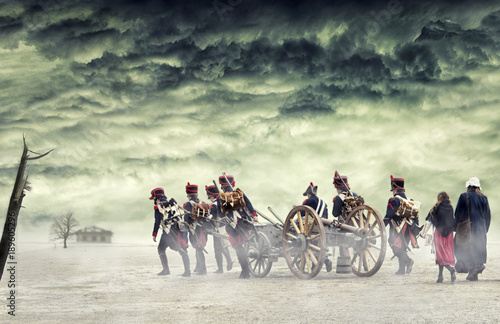 Fotografia Napoleonic soldiers and women marching and pulling a cannon in plain land, countryside with stormy clouds