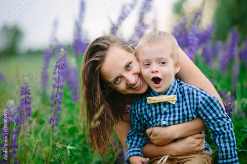 Beautiful woman and her cute little son are smiling, on lupine field