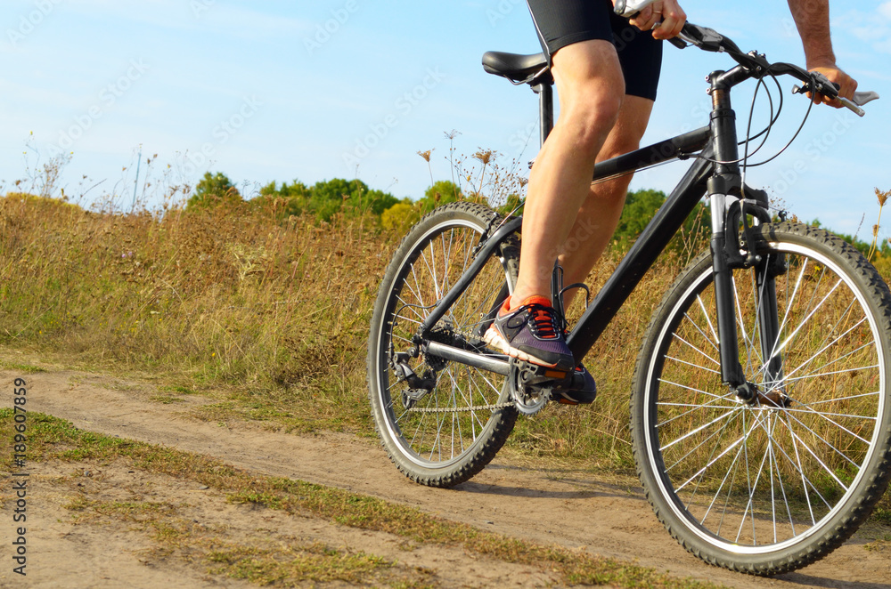 Male cyclist driving by rural dirt road outdoors. Low angle view Male cyclist driving by rural dirt road outdoors. Low angle view