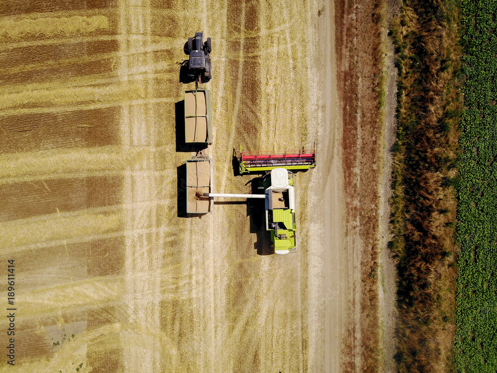 Top view from flying drone of large professional combine harvester loading wheat into the tank of the tractor-trailer on the field. Top view from flying drone of large professional combine harvester loading wheat into the tank of the tractor-trailer on the field.