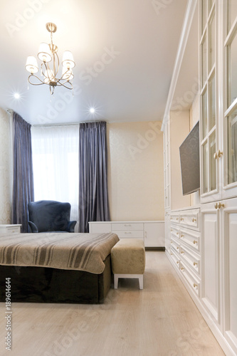 Спальня в светлых тонах с темной кроватью и синими шторами