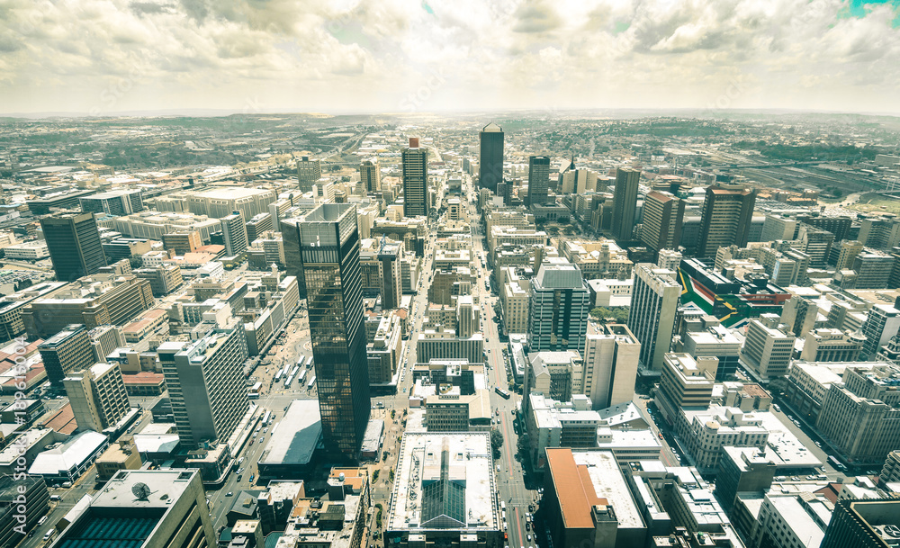 Fototapeta premium Skyline z lotu ptaka na drapacze chmur w biznesowej dzielnicy Johannesburga - koncepcja architektury z nowoczesnymi budynkami panoramę w największym mieście RPA z flagą południowoafrykańską namalowaną na ścianach