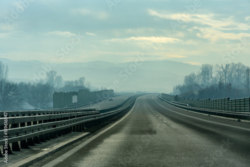 Two line wide highway on a cloudy winter day leading to the mountains through rural landscape