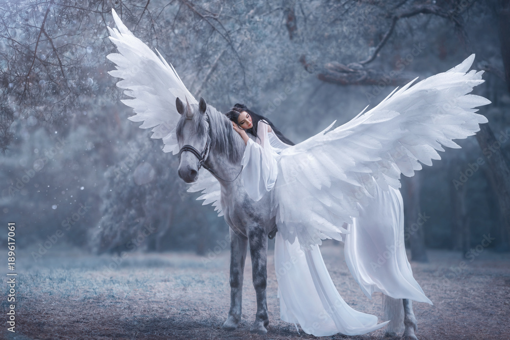 Obraz premium Piękna, młoda elfka, spacerująca z jednorożcem. Ma na sobie niesamowitą lekką, białą sukienkę. Dziewczyna leży na koniu. Śpiąca Królewna. Fotografia artystyczna