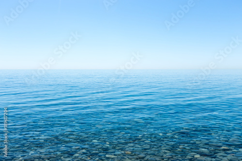 Beautiful seascape with a view of the horizon and a cloudless sky. Small smooth stones lying on the sea bottom with clear water on the shore