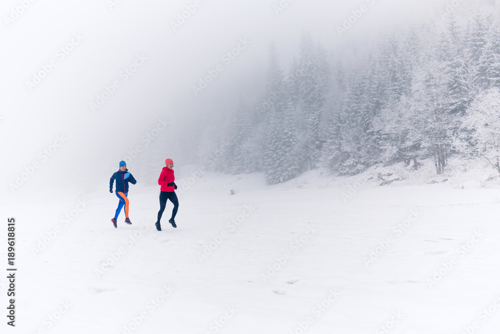 Two women trail running on snow in winter mountains