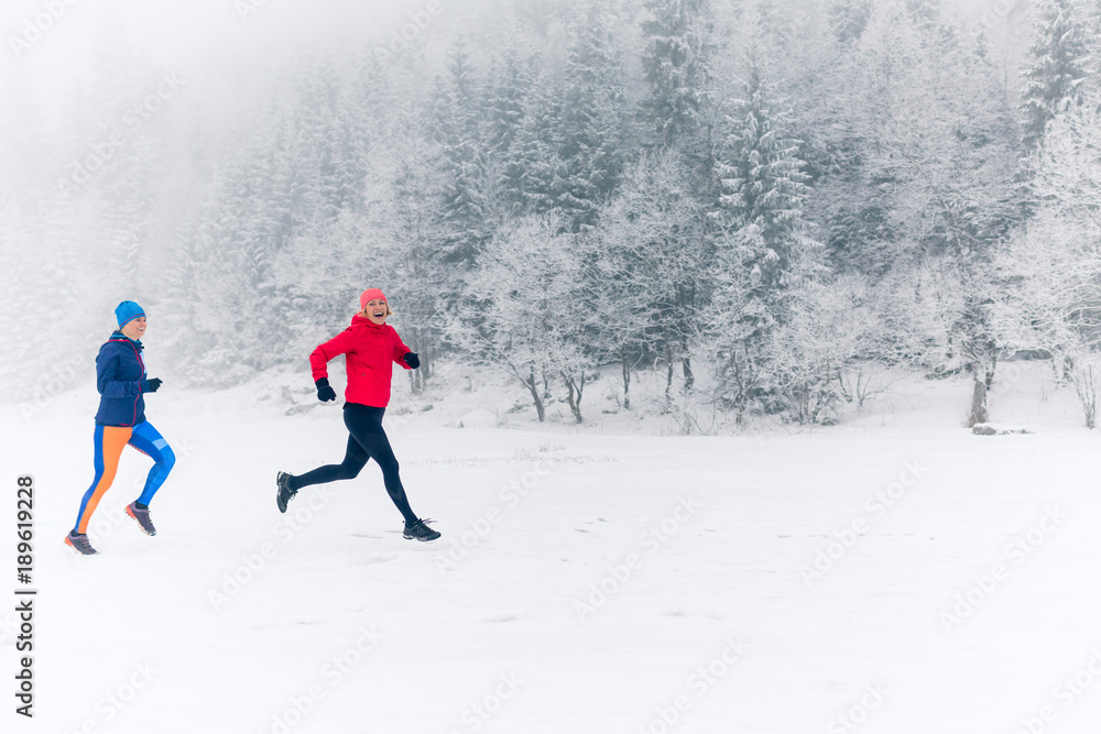 Two women trail running on snow in winter mountains